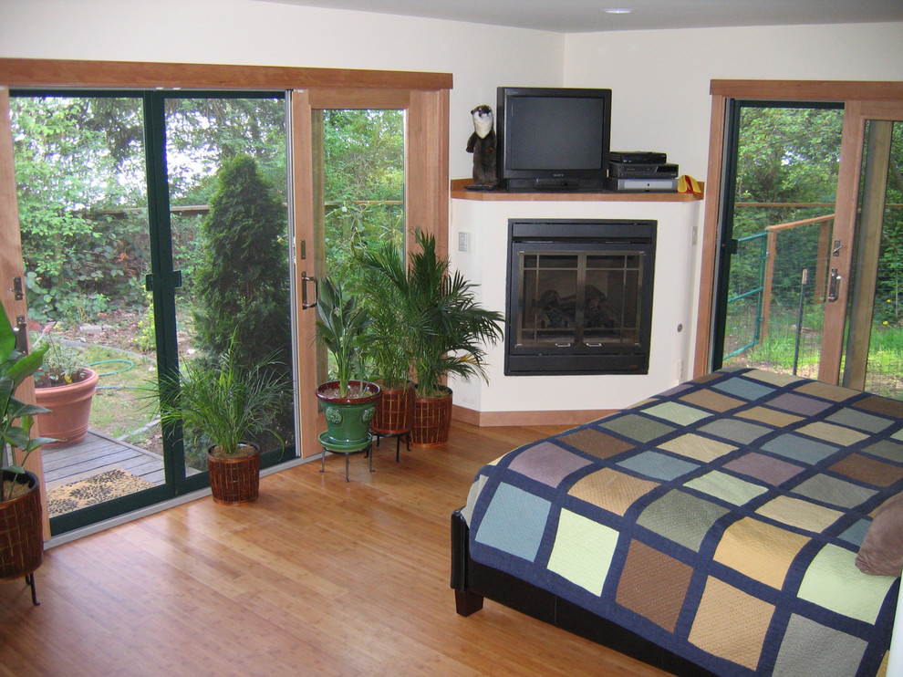 Foto de dormitorio principal contemporáneo de tamaño medio con paredes blancas, suelo de madera clara, chimenea de esquina, marco de chimenea de yeso y suelo beige