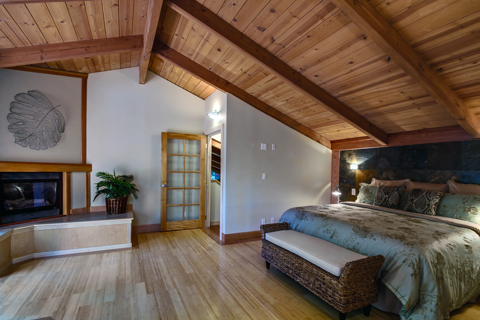 Aménagement d'une grande chambre parentale craftsman avec un mur beige, parquet en bambou, une cheminée d'angle et un manteau de cheminée en bois.