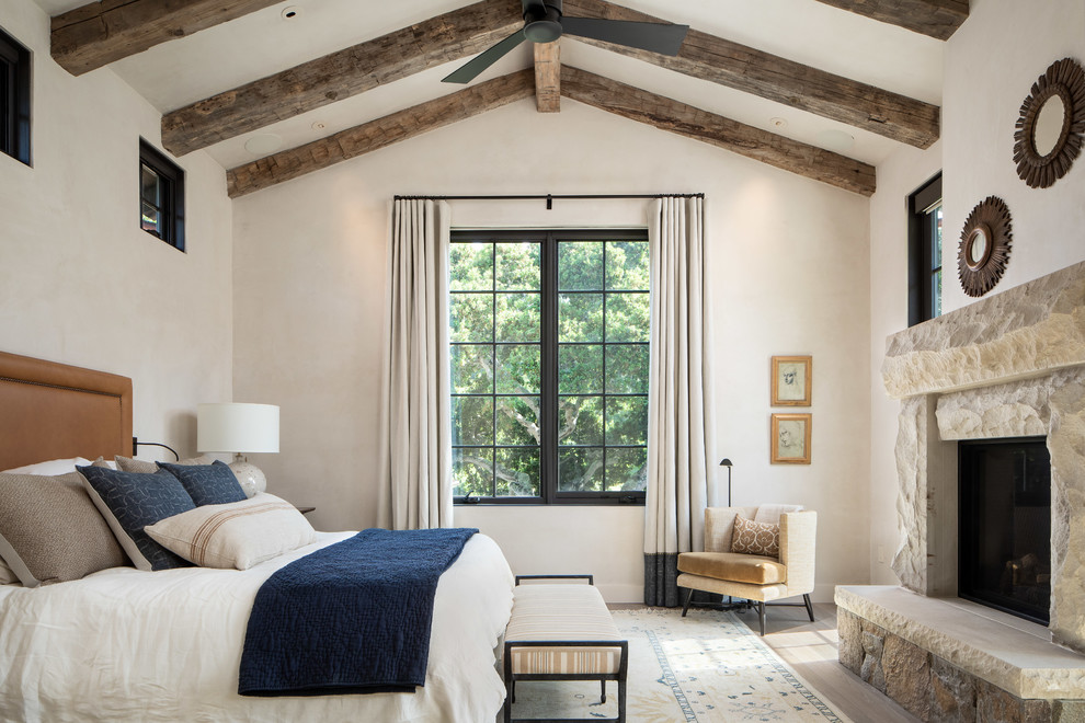 Großes Mediterranes Hauptschlafzimmer mit beiger Wandfarbe, hellem Holzboden, Kamin, Kaminumrandung aus Stein und beigem Boden in Orange County