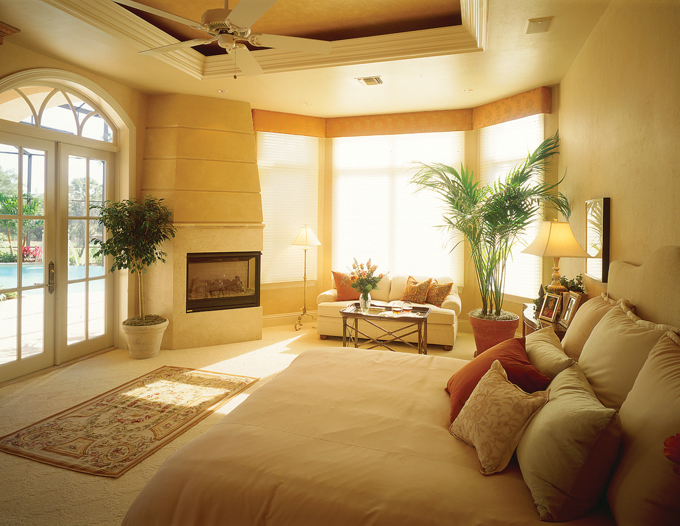 Großes Mediterranes Hauptschlafzimmer mit beiger Wandfarbe, Teppichboden, Kamin und Kaminumrandung aus Stein in Miami