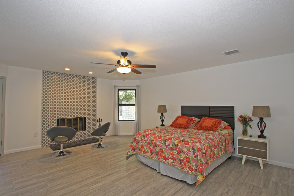 他の地域にある広いトランジショナルスタイルのおしゃれな主寝室 (白い壁、磁器タイルの床、標準型暖炉、タイルの暖炉まわり、茶色い床) のレイアウト