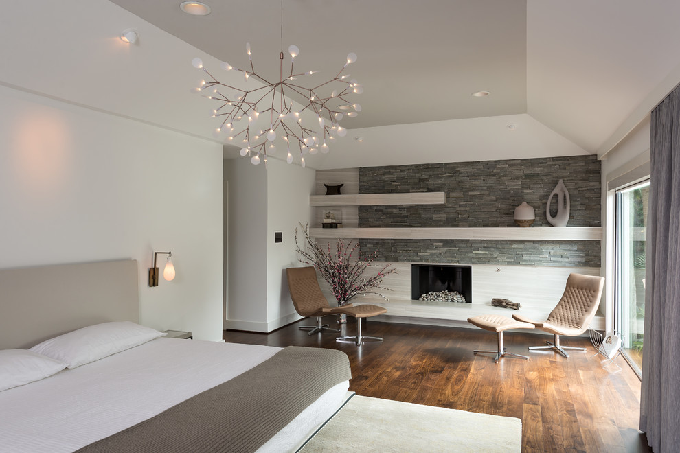 Großes Modernes Hauptschlafzimmer mit weißer Wandfarbe, braunem Holzboden, Kamin und Kaminumrandung aus Stein in Houston