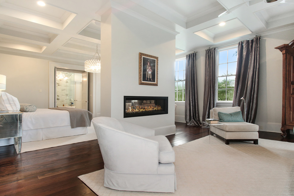Large traditional master bedroom in New Orleans with white walls, dark hardwood flooring, a two-sided fireplace and brown floors.