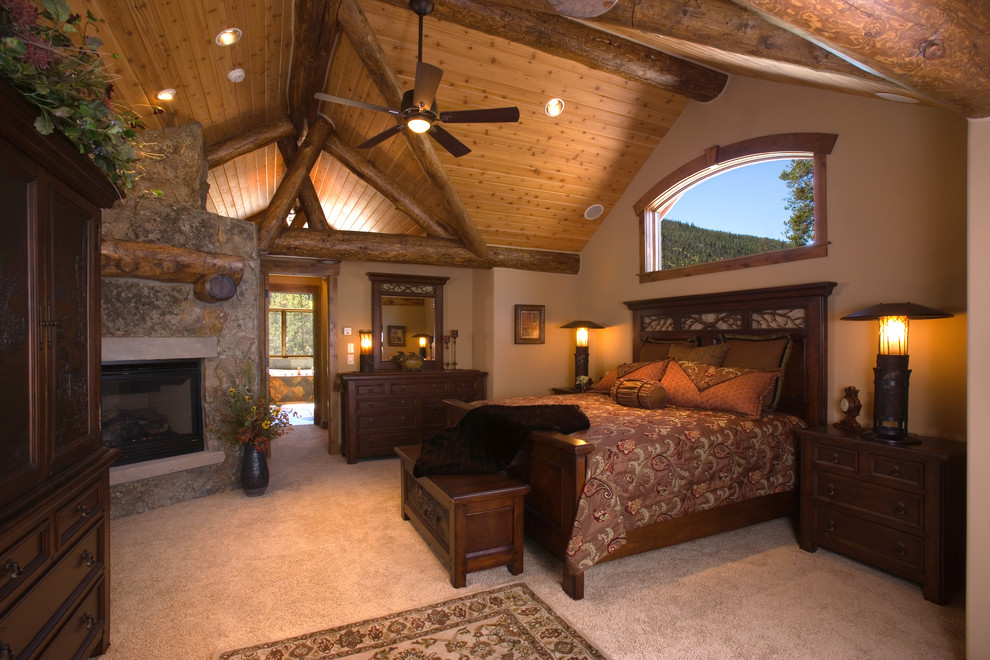 Modelo de dormitorio rústico con paredes beige, moqueta, marco de chimenea de piedra y chimenea de esquina