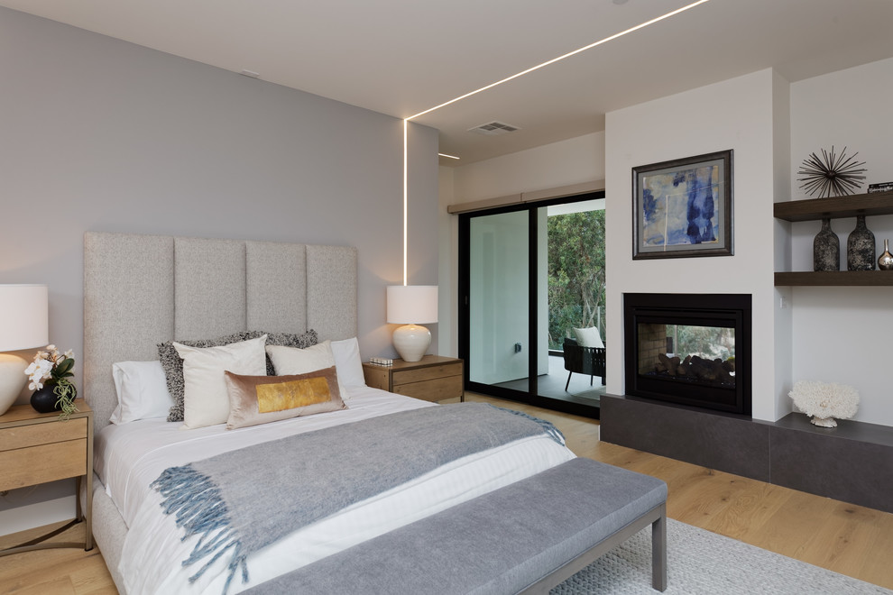 Diseño de dormitorio principal moderno grande con paredes blancas, suelo de madera clara, chimenea de doble cara y suelo beige