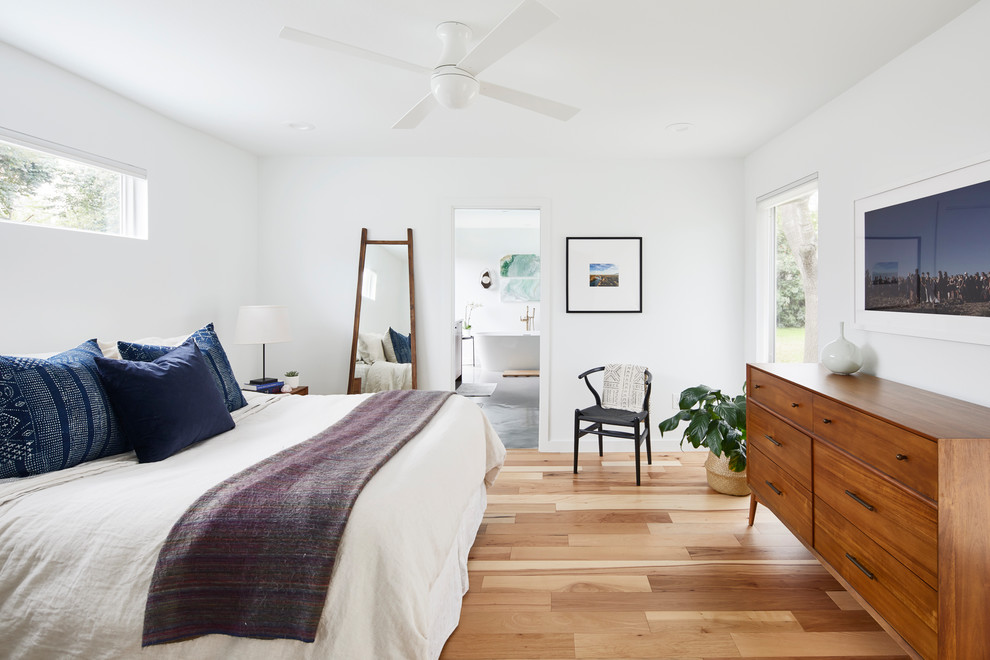 オースティンにある広いコンテンポラリースタイルのおしゃれな主寝室 (白い壁、淡色無垢フローリング、暖炉なし、茶色い床、照明) のインテリア