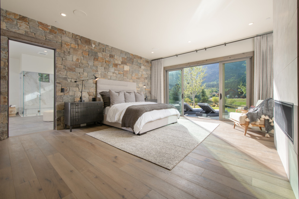 Rustikales Hauptschlafzimmer mit hellem Holzboden, Kamin, Kaminumrandung aus Beton und braunem Boden