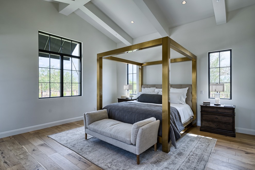 フェニックスにある広い地中海スタイルのおしゃれな主寝室 (白い壁、無垢フローリング、標準型暖炉、漆喰の暖炉まわり、茶色い床)
