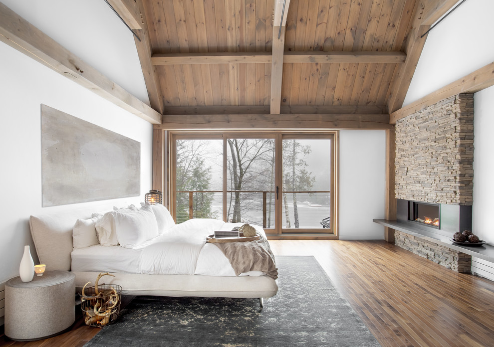 Ejemplo de dormitorio rústico con paredes blancas, suelo de madera en tonos medios, chimenea lineal y suelo marrón