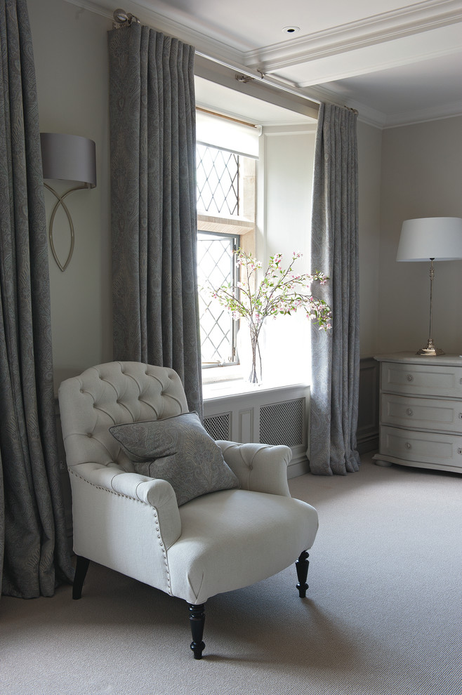 Expansive farmhouse master and grey and silver bedroom in Gloucestershire with beige walls and carpet.