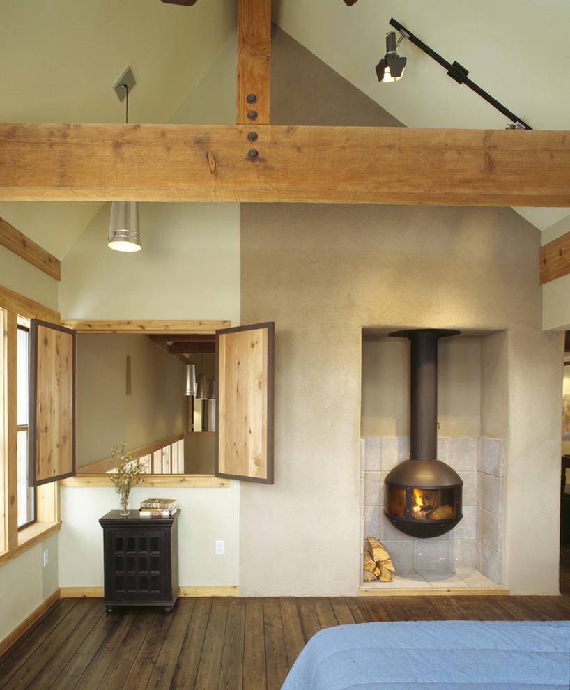 Ejemplo de dormitorio rural con paredes blancas, suelo de madera oscura y estufa de leña