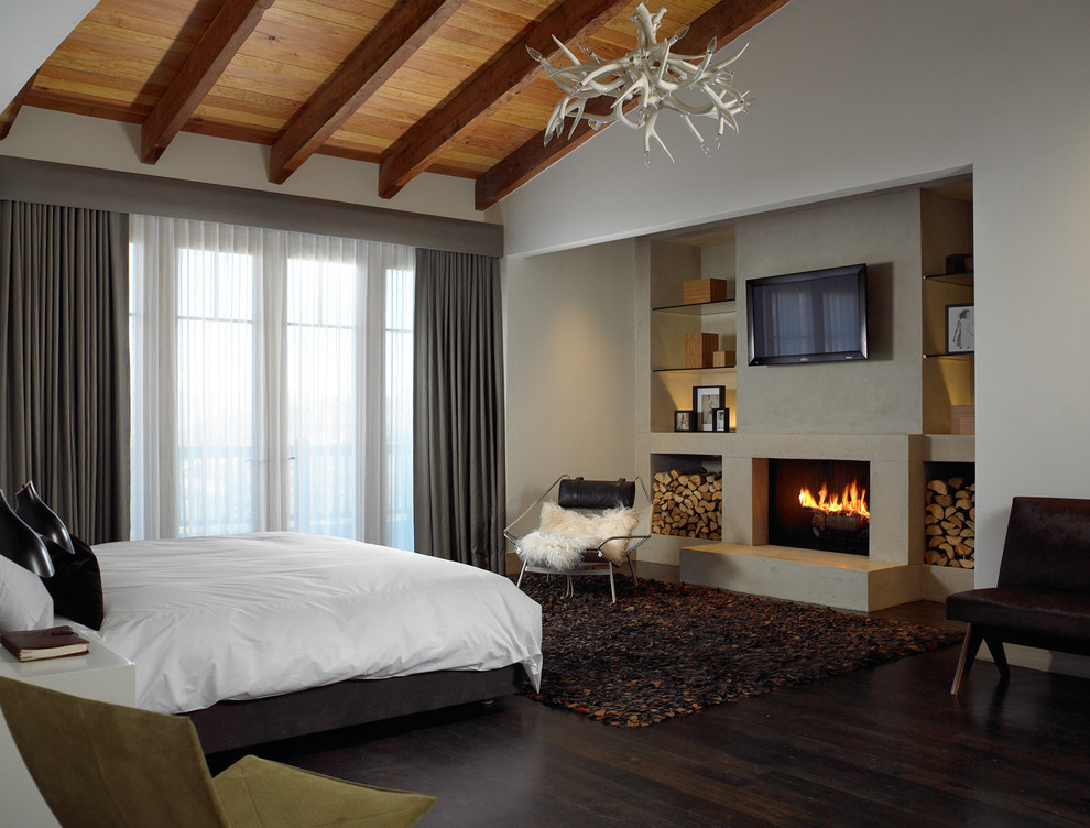 Cette image montre une chambre d'amis chalet de taille moyenne avec un mur blanc, parquet foncé, une cheminée standard, un manteau de cheminée en plâtre et un sol marron.