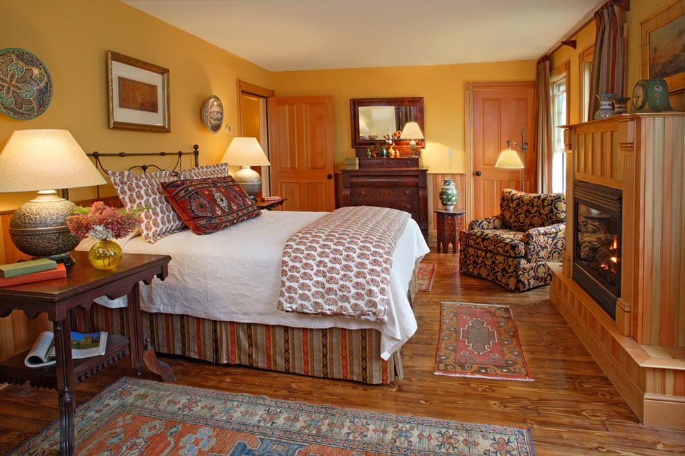 Imagen de dormitorio principal rústico de tamaño medio con paredes amarillas, suelo de madera en tonos medios, todas las chimeneas y marco de chimenea de madera