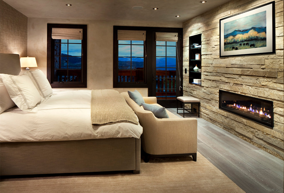 This is an example of a rustic master bedroom in Other with beige walls, dark hardwood flooring, a ribbon fireplace and a stone fireplace surround.