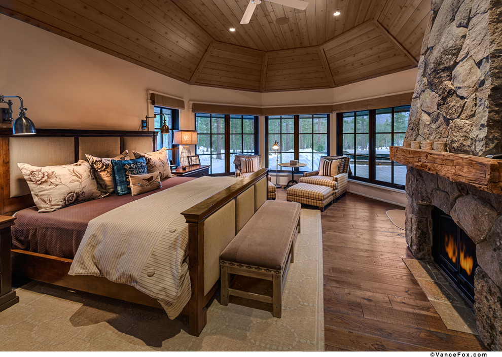 Cette image montre une grande chambre d'amis craftsman avec un mur beige, parquet foncé, une cheminée standard et un manteau de cheminée en pierre.