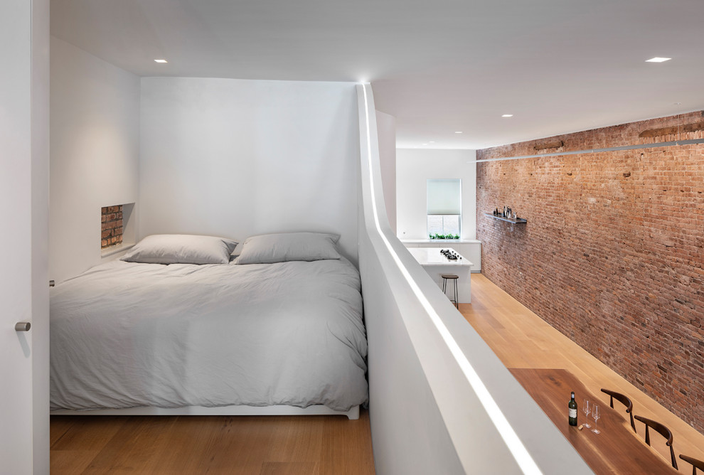 Ejemplo de dormitorio tipo loft actual pequeño con paredes blancas, suelo de madera en tonos medios y suelo marrón