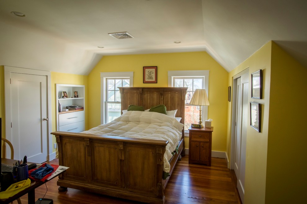 Cette image montre une chambre mansardée ou avec mezzanine traditionnelle de taille moyenne avec un mur jaune, un sol en bois brun, aucune cheminée et un sol marron.