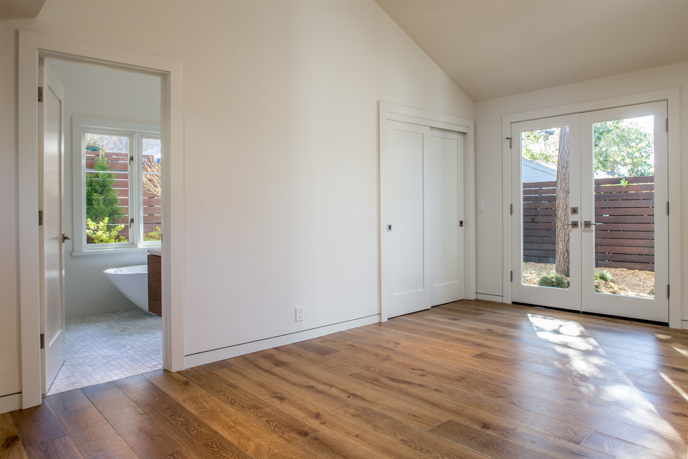 Idée de décoration pour une chambre parentale minimaliste de taille moyenne avec un mur blanc, un sol en bois brun et aucune cheminée.