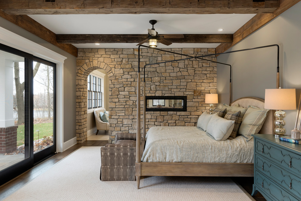 ミネアポリスにあるトラディショナルスタイルのおしゃれな主寝室 (グレーの壁、濃色無垢フローリング、両方向型暖炉、石材の暖炉まわり、アクセントウォール) のレイアウト