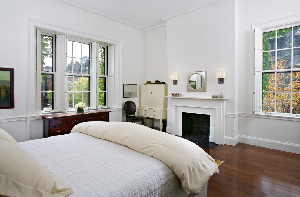 Example of a large classic medium tone wood floor bedroom design in Boston with white walls, a standard fireplace and a brick fireplace