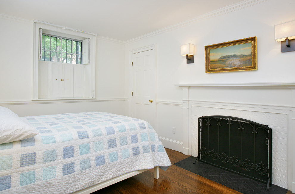 Foto di una grande camera da letto chic con pareti bianche, pavimento in legno massello medio, camino classico e cornice del camino in mattoni
