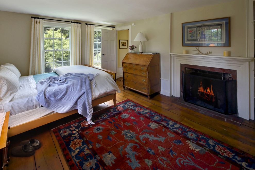 This is an example of a large classic master bedroom in Portland Maine with beige walls, medium hardwood flooring, a standard fireplace and a plastered fireplace surround.