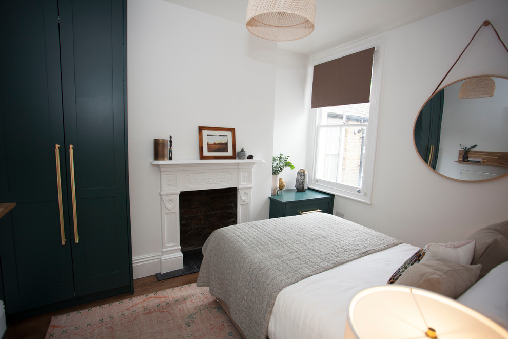 Cette image montre une petite chambre parentale design avec un mur gris, parquet foncé, une cheminée standard, un manteau de cheminée en plâtre et un sol marron.