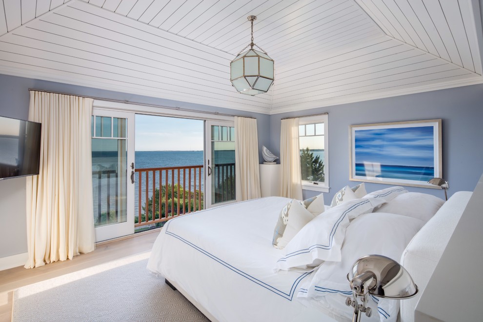 Modelo de dormitorio principal marinero grande sin chimenea con paredes azules, suelo de madera clara y suelo beige