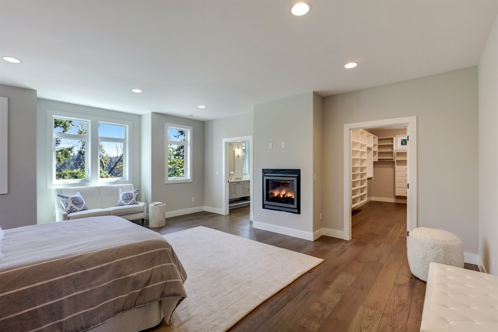 Cette photo montre une grande chambre d'amis tendance avec un mur gris, un sol en bois brun, une cheminée standard, un manteau de cheminée en plâtre et un sol gris.