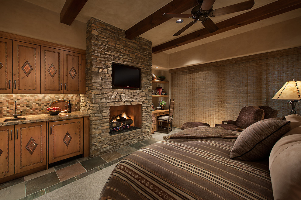 Cette photo montre une chambre d'amis sud-ouest américain de taille moyenne avec un mur beige, un sol en ardoise, une cheminée standard et un manteau de cheminée en pierre.