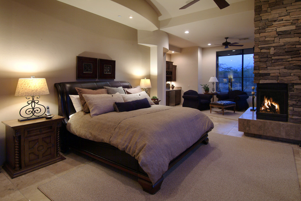 Diseño de dormitorio principal de estilo americano grande con marco de chimenea de piedra, chimenea de esquina, paredes beige, suelo de travertino y suelo marrón