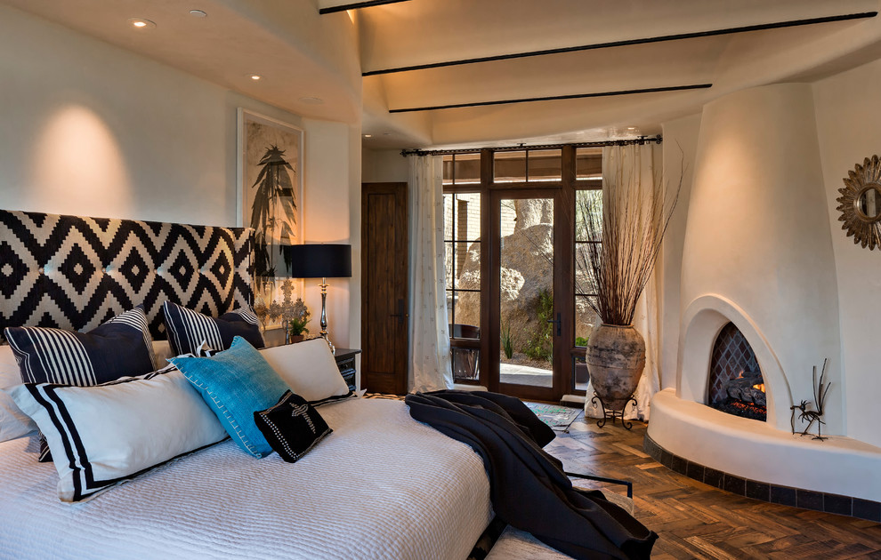 Ejemplo de dormitorio principal de estilo americano de tamaño medio con paredes beige, marco de chimenea de yeso, suelo de madera oscura, chimenea de esquina y suelo marrón