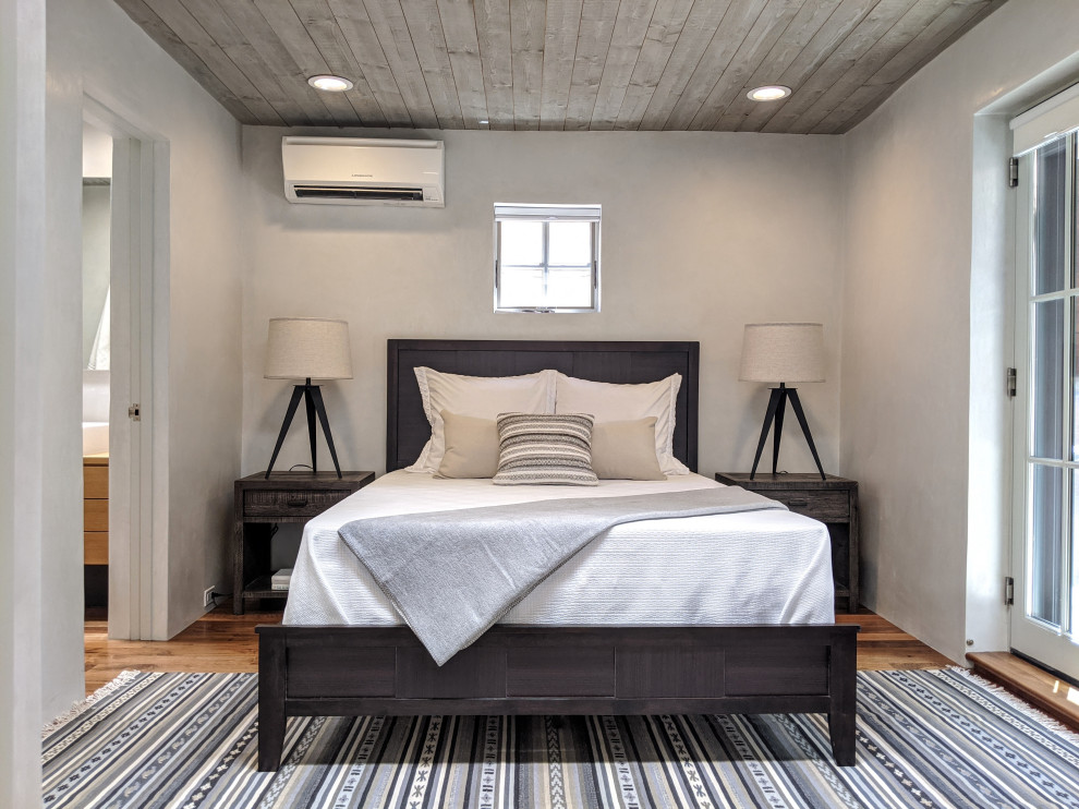 Modelo de habitación de invitados de estilo americano pequeña sin chimenea con paredes blancas, suelo de madera en tonos medios, suelo marrón y madera