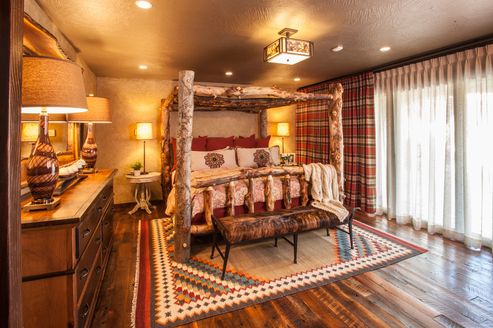 Ejemplo de dormitorio principal rural grande con paredes beige, suelo de madera en tonos medios y marco de chimenea de piedra