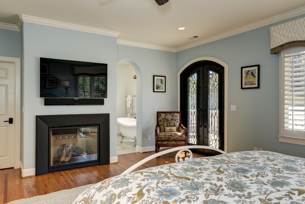 Modelo de dormitorio principal clásico grande con paredes azules, suelo de madera en tonos medios, todas las chimeneas y marco de chimenea de piedra