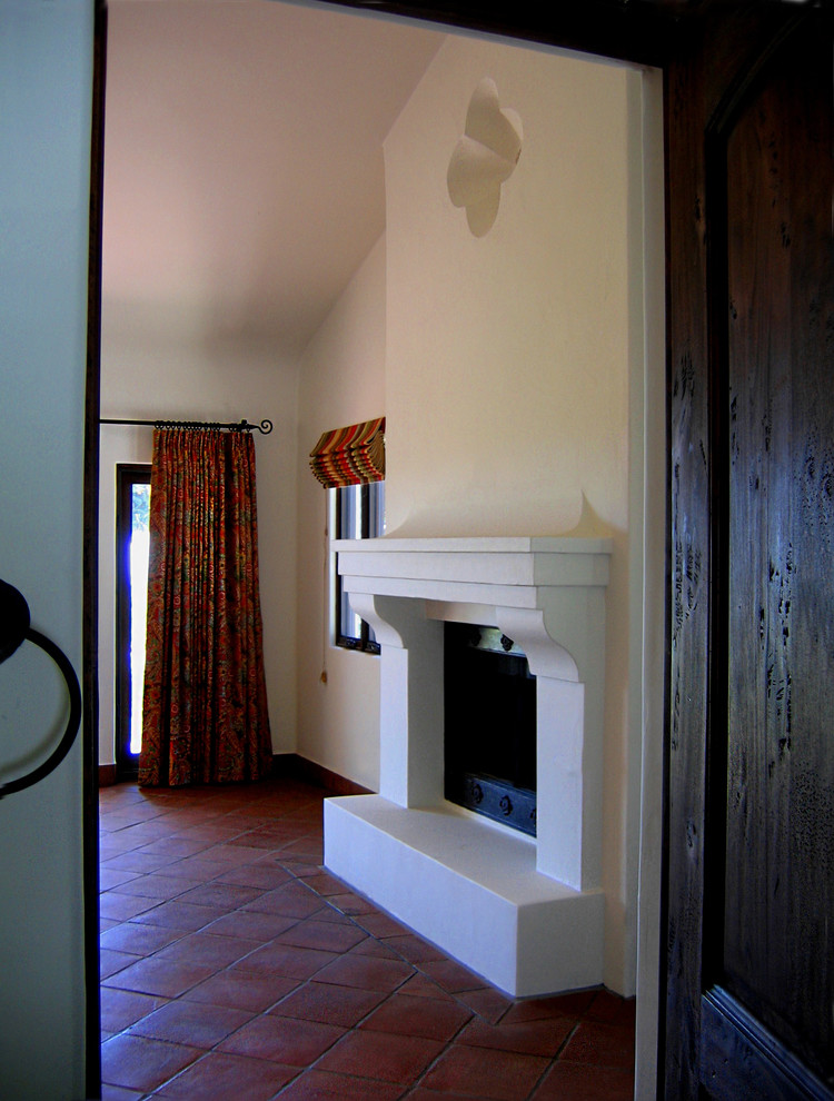 Стильный дизайн: хозяйская спальня среднего размера в средиземноморском стиле с белыми стенами, полом из терракотовой плитки, стандартным камином и красным полом - последний тренд