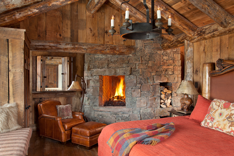 他の地域にあるラスティックスタイルのおしゃれな寝室 (濃色無垢フローリング、石材の暖炉まわり、コーナー設置型暖炉)