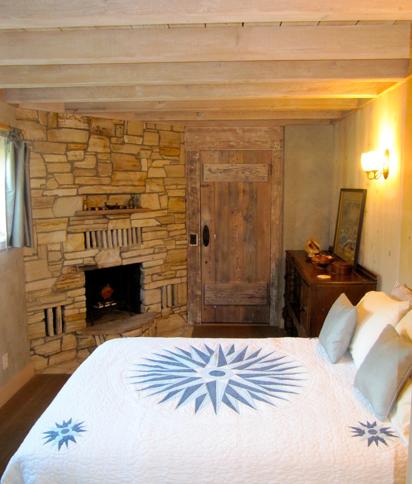 Diseño de habitación de invitados mediterránea pequeña con paredes beige, suelo de madera en tonos medios, chimenea de esquina, marco de chimenea de piedra y suelo marrón