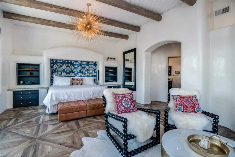 アルバカーキにある広いトランジショナルスタイルのおしゃれな主寝室 (白い壁、コーナー設置型暖炉、漆喰の暖炉まわり、茶色い床、磁器タイルの床) のレイアウト