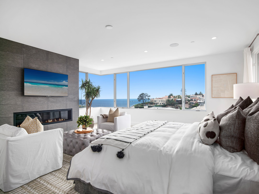 Ejemplo de dormitorio costero grande con paredes blancas, moqueta, chimenea lineal, marco de chimenea de baldosas y/o azulejos y suelo beige