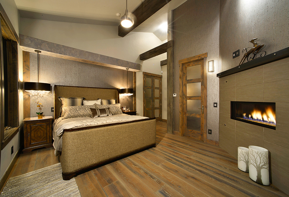Ejemplo de dormitorio principal rural grande con paredes beige, suelo de madera en tonos medios, chimenea lineal, marco de chimenea de baldosas y/o azulejos y suelo marrón