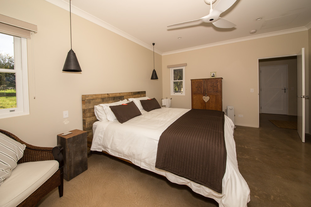 Ejemplo de dormitorio principal de estilo de casa de campo de tamaño medio con paredes beige, suelo de cemento, marco de chimenea de piedra y estufa de leña
