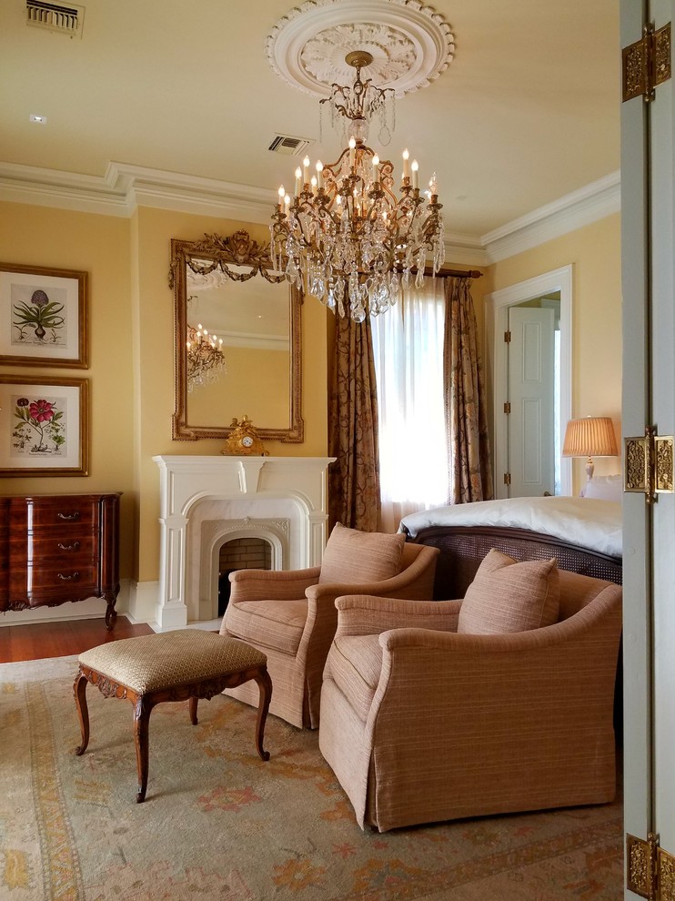 ニューオリンズにある広いトラディショナルスタイルのおしゃれな主寝室 (黄色い壁、無垢フローリング、標準型暖炉、木材の暖炉まわり、茶色い床)