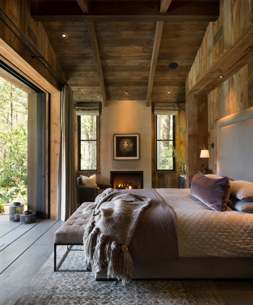На фото: хозяйская спальня в стиле кантри с коричневыми стенами, бетонным полом, стандартным камином и фасадом камина из штукатурки с