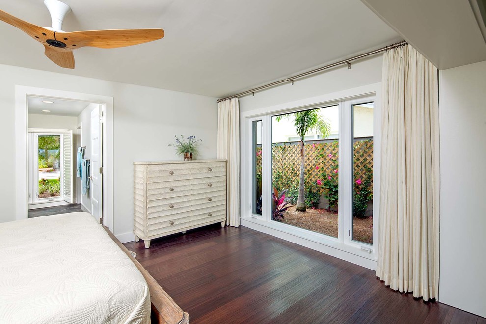 Ejemplo de dormitorio principal tropical de tamaño medio sin chimenea con paredes beige y suelo de madera oscura