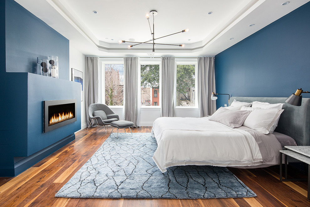 Modernes Hauptschlafzimmer mit blauer Wandfarbe, Kaminumrandung aus Metall, braunem Holzboden und Gaskamin in New York