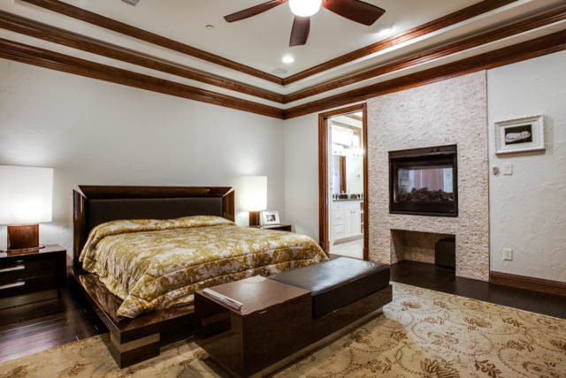 Example of a large classic master dark wood floor bedroom design in Dallas with white walls, a two-sided fireplace and a stone fireplace