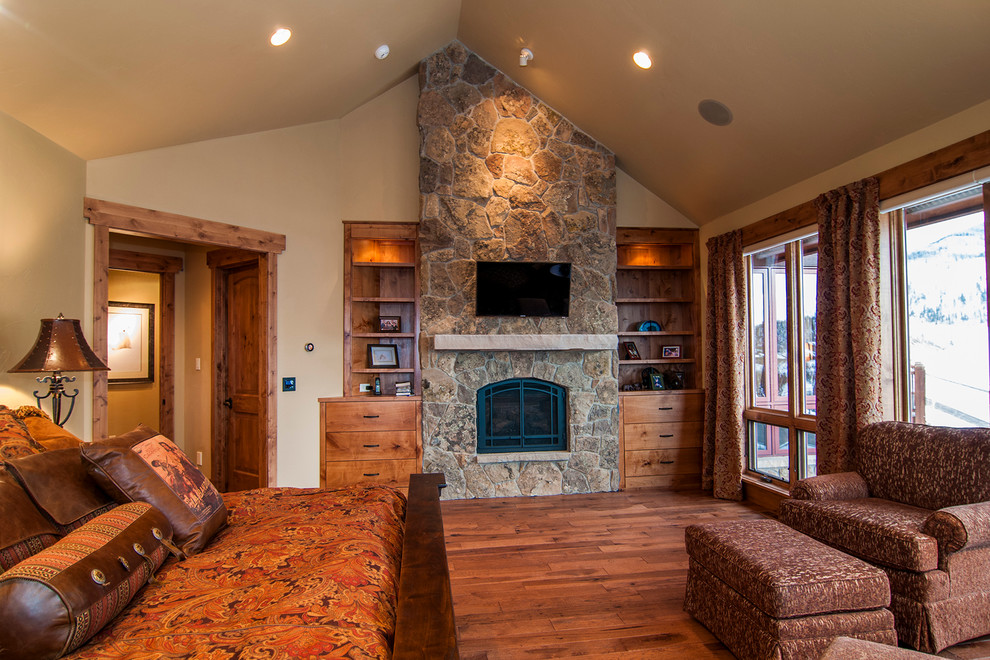 Großes Uriges Hauptschlafzimmer mit beiger Wandfarbe, braunem Holzboden, Kamin und Kaminumrandung aus Stein in Denver