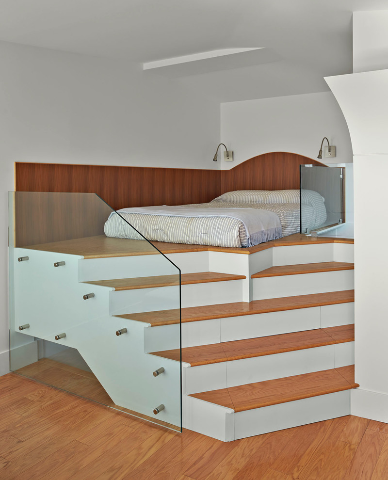 Modelo de dormitorio tipo loft contemporáneo con paredes blancas y suelo de madera en tonos medios