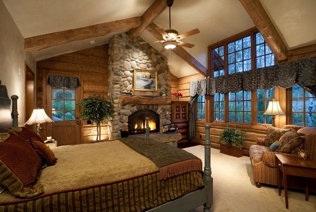 This is an example of a large rustic master bedroom in Denver with a standard fireplace, a stone fireplace surround, beige walls and medium hardwood flooring.